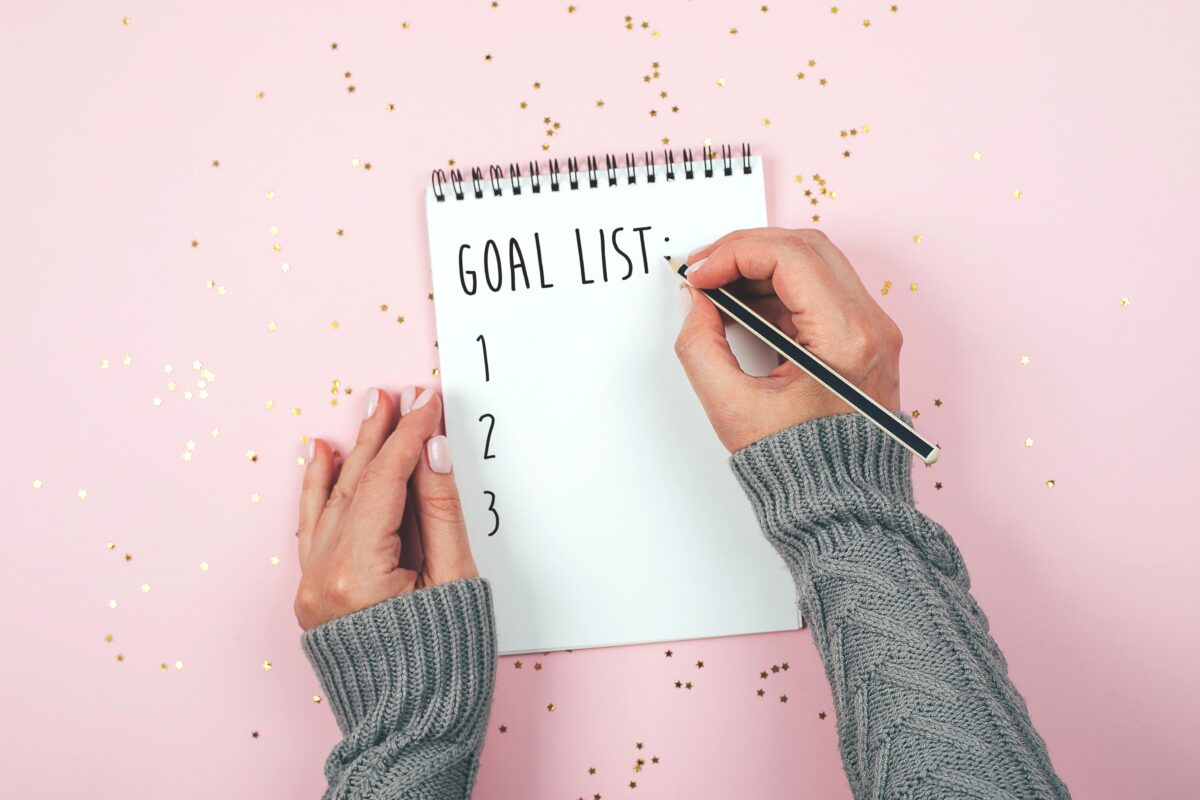 Person writing down their goals in a notebook with a pen