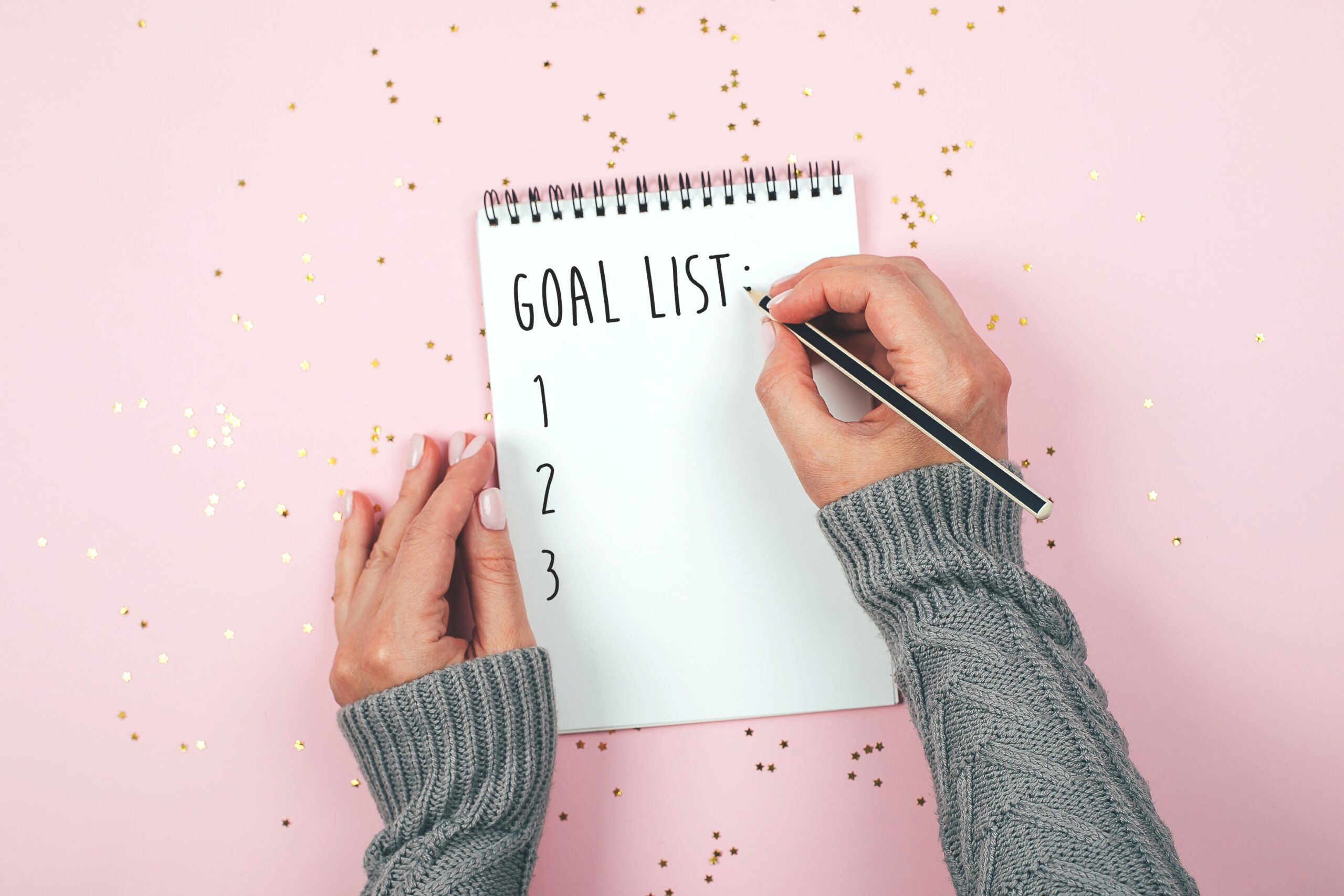 Person writing down their goals in a notebook with a pen