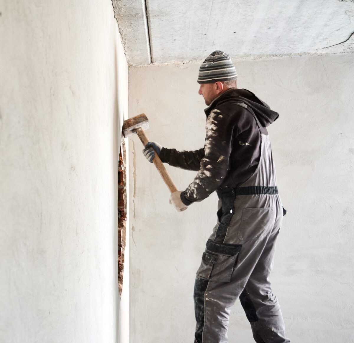 A man is breaking through a brick wall with a sledgehammer.