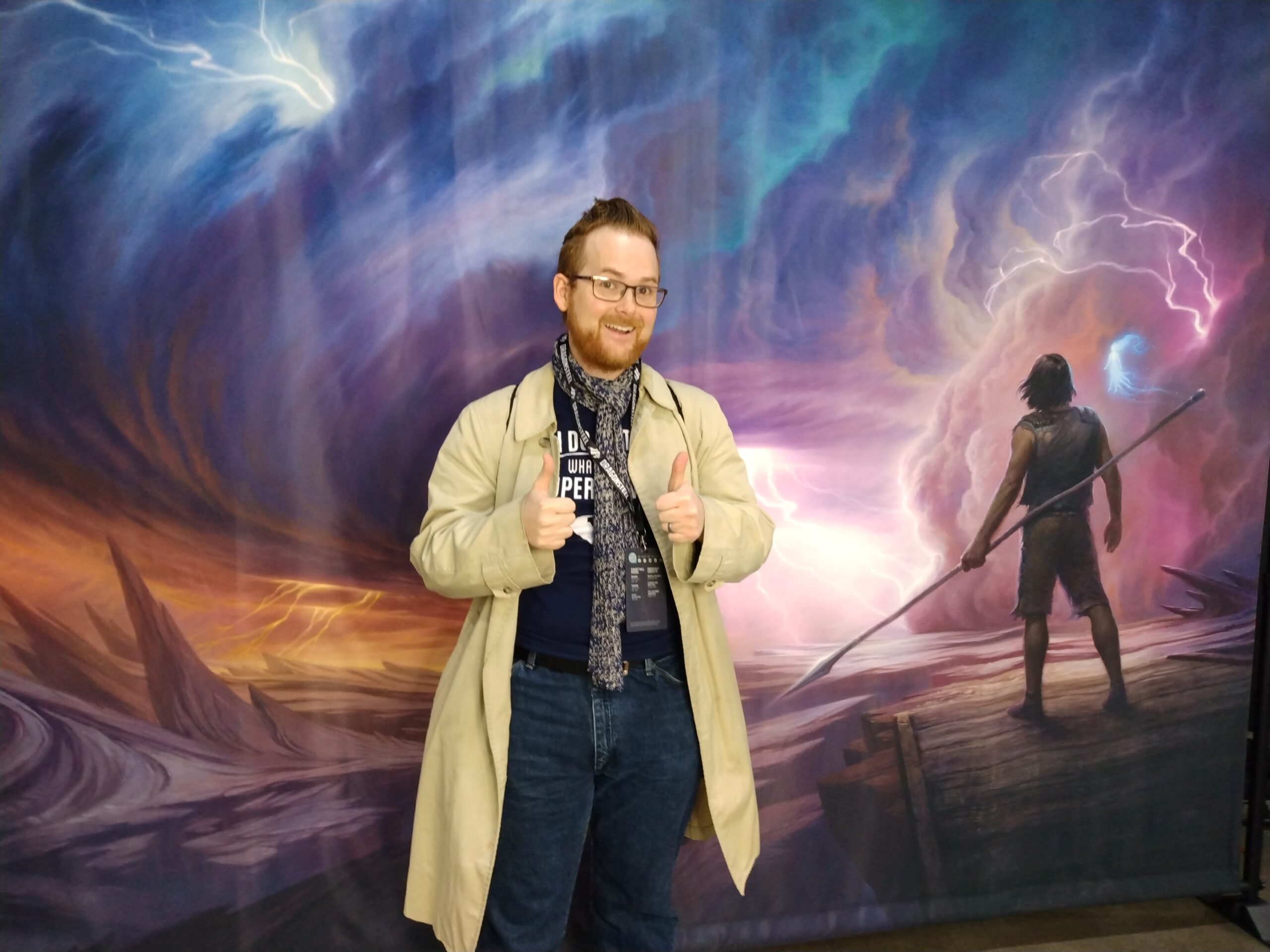 Timothy Kuhn stands with a big grin on his face. Behind him, Kaladin and Sil stare across the desolate Shattered Plains, a Highstorm bearing down on them.